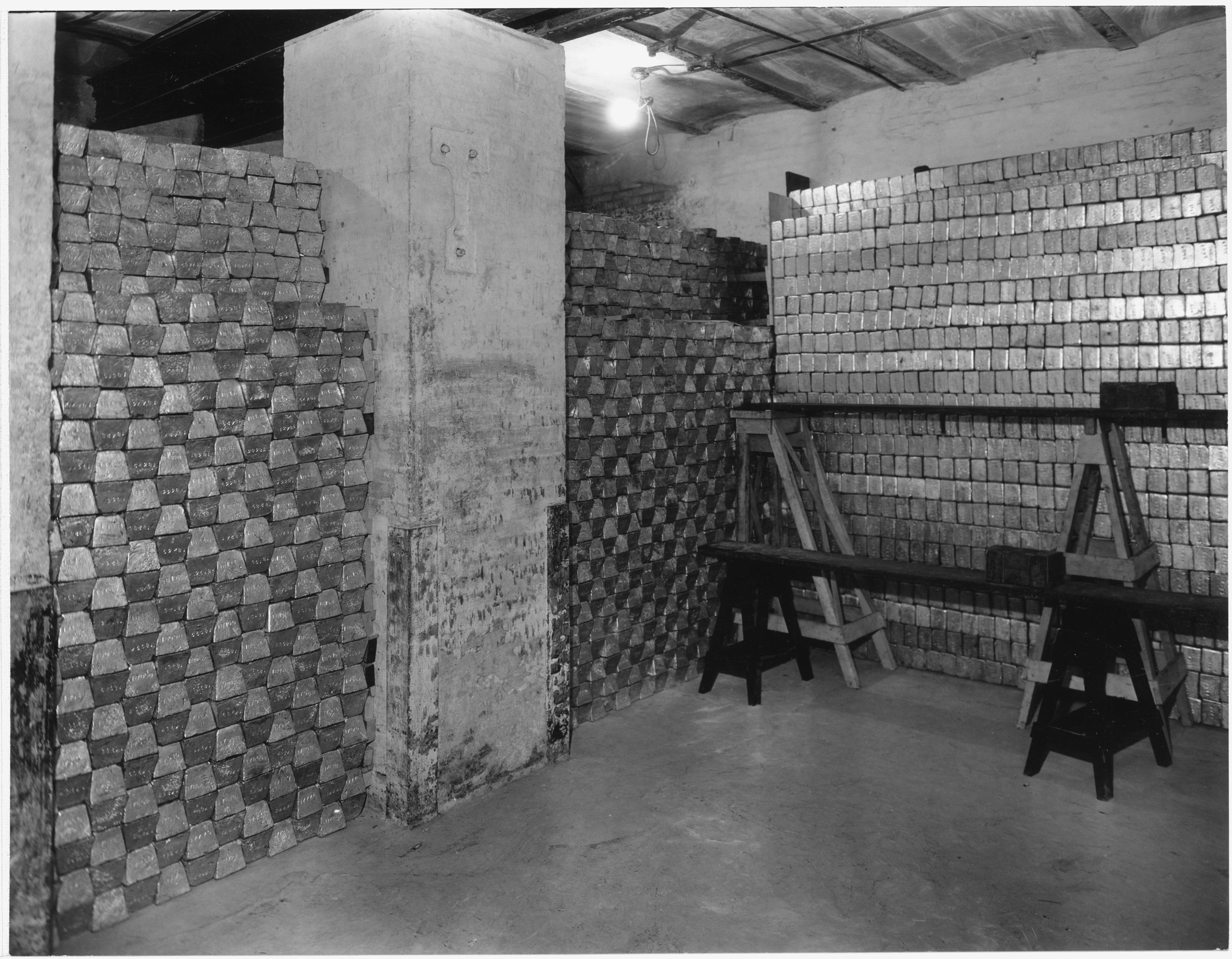 Alt text: `A vault filled with rows of gold bars in a historical photograph dating to circa 1935.`