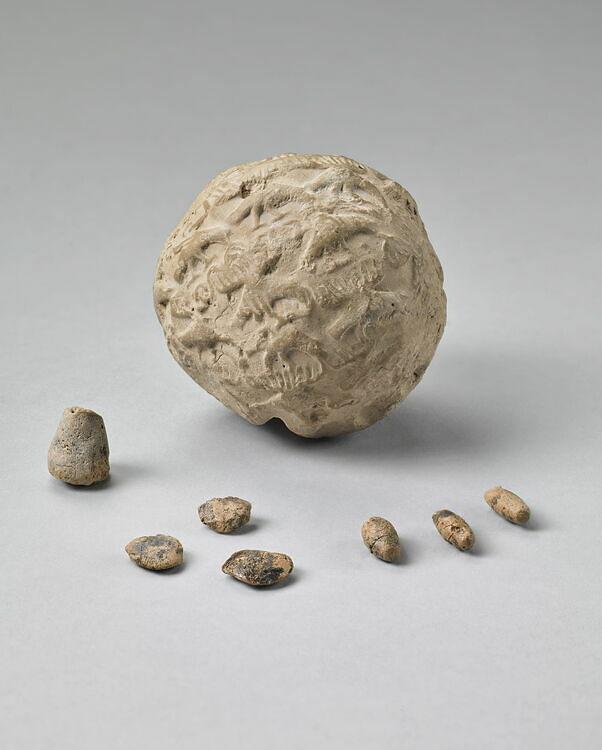 Small clay accounting tokens of different shapes, with incised lines and markings, displayed on a museum shelf.